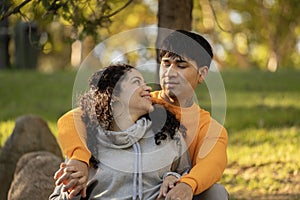 Latin couple hugging and flirting in an urban park sitting in the grass and looking each other