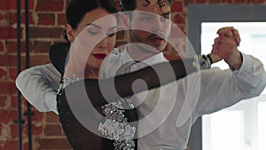 Latin dances - man and woman training their dance movements in the studio with brick walls - the man counting the tempo