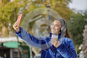 Latin girl with headphones taking a selfie with her mobile phone in a public park