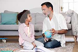 Latin Grandpa Talking To Grandson Holding World Globe At Home