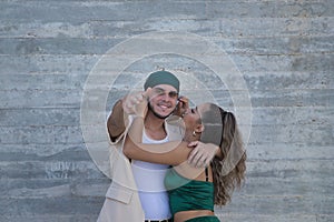 Latin and Hispanic boy and girl couple, young and nonconformist, embracing, while he makes a gun shape with hand pointing photo