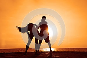 latin hispanic couple is dancing bachata above sea on summer beach. Sunset over water.Two silhouettes against the sun. Just