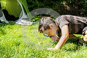 latin kid checking the grass with magnifying glass on a camping trip