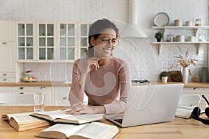 Latin lady reading book on laptop distracted from paper literature