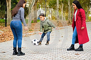 Latin lesbian couple playing football with their son at a park.