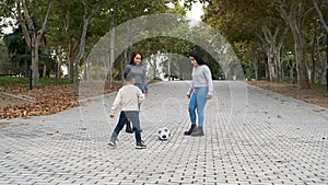 Latin lesbian couple playing football with their son at a park.