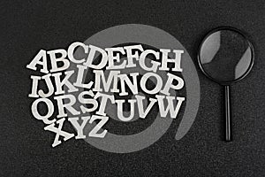 Latin letters in alphabetical order from A to Z on black background. Magnifying glass