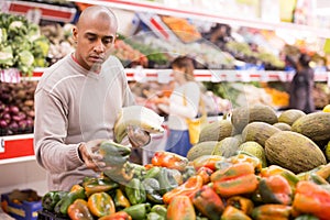 Latin man choosing sweet pepper and woman near choosing other vegetables