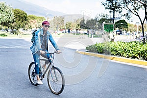 Latin man in Jeans riding a bicycle in a city with a red cap and glasses
