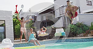 Latin man jumping into swimming pool and laughing with friends at pool party