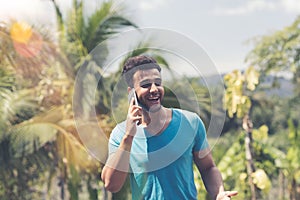 Latin Man Making Phone Call Over Tropical Forest And Blue Sky Background Happy Smiling Mix Race Guy