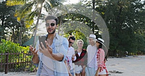 Latin Man Making Video Call Using Cell Smart Phone People Group Talking In Tropical Palm Tree Park