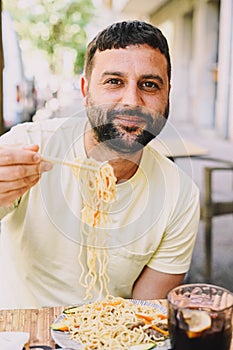 Latin man sitting on a terrace eating sushi and Japanese noodles