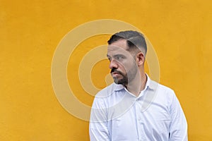 Latin man standing in front of a yellow wall. He is looking to the side with seriousness