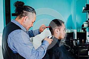 Latin man stylist cutting hair to a client in a barber shop in Mexico photo