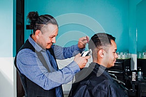 Latin man stylist cutting hair to a client in a barber shop in Mexico photo