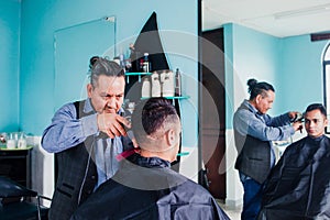 Latin man stylist cutting hair to a client in a barber shop in Mexico photo