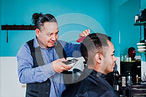 Latin man stylist cutting hair to a client in a barber shop in Mexico photo