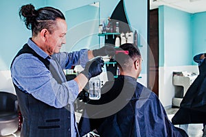 Latin man stylist cutting hair to a client in a barber shop in Mexico photo