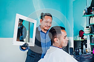 Latin man stylist cutting hair to a client and holding a mirror in a barber shop in Mexico photo