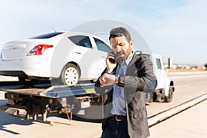 Latin man talking and looking at his watch next to a tow truck