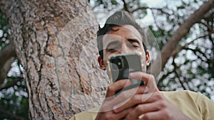 Latin man texting cellphone in green park closeup. Carefree guy browsing online