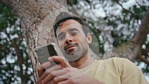 Latin man texting cellphone in green park closeup. Carefree guy browsing online