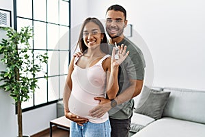 Latin man and woman couple hugging each other holding key of new house expecting baby at home