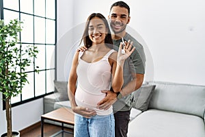 Latin man and woman couple hugging each other holding key of new house expecting baby at home