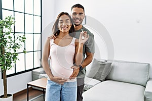 Latin man and woman couple hugging each other holding key of new house expecting baby at home