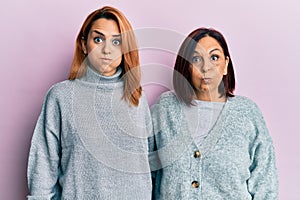 Latin mother and daughter wearing casual clothes puffing cheeks with funny face