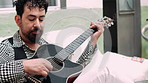Latin musician playing the guitar sitting on a sofa. Passionate musician with his guitar