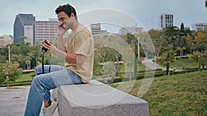 Latin photographer talking smartphone in green park. Happy carefree guy calling