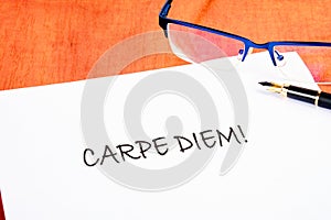 The Latin phrase Carpe Diem, a quote from Horace, means seize the moment. Live in the present written on a white piece of paper on