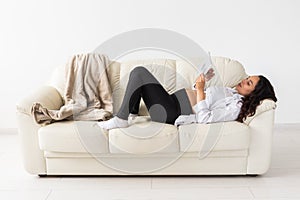 Latin pregnant woman using tablet computer while lying on sofa at home. Pregnancy and information for parenthood concept