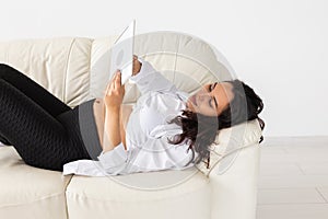 Latin pregnant woman using tablet computer while lying on sofa at home. Pregnancy and information for parenthood concept