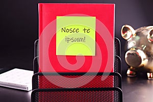 Latin proverb NOSCE TE IPSUM (know yourself) on a yellow sticker glued to a red notebook photo