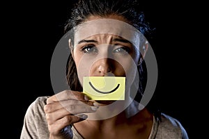 Latin sad depressed latin girl holding paper hiding her mouth behind fake drawn smile photo