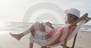 Latin senior hispanic man relaxing on sunbed on beach at sunset, reading book