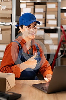 Latin smiling young woman working at small business commerce doing happy thumbs up gesture, looking at the camera