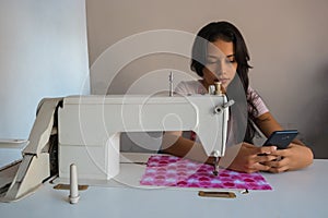 Latin tailor in his workshop smiling as he sees something on his phone