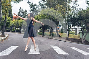 Latin teenage dancer girl with black dress walking elegantly with ballet shoes on a pedestrian crossing in the street