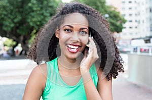 Latin woman with curly hair and green shirt at phone in city