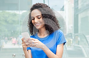 Latin woman with curly hair typing message at phone