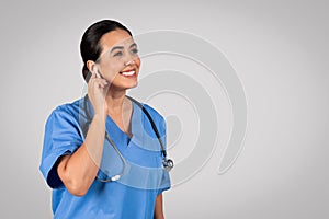 Latin woman doctor with earpad, consulting patient online over grey background, copy space photo