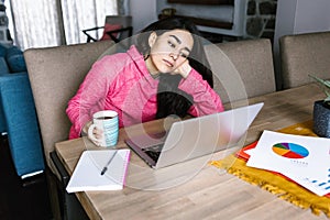 Latin woman in front of her laptop staring at the screen, bored, sleepy, tired in a home office concept in Mexico Latin America