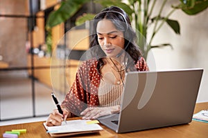 Latin woman with headset writing notes during video call