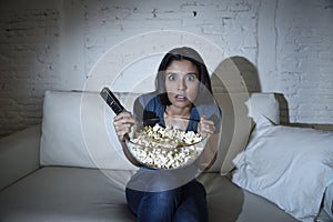 Latin woman at home sofa couch in living room watching television covering eyes horrified photo