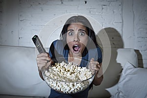 Latin woman at home sofa couch in living room watching television covering eyes horrified photo