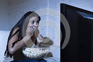 Latin woman at home sofa couch in living room watching television scary horror movie or suspense thriller